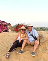 happy guests relaxing on sand sunes with camels in backdrop